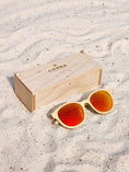 Load image into Gallery viewer, Maple Wooden sunglasses with red polarized lenses and a box on sandy beach.