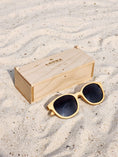 Load image into Gallery viewer, Maple Wooden sunglasses with black polarized lenses and a box on sandy beach.