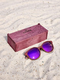 Load image into Gallery viewer, Purpleheart wooden sunglasses with purple polarized lenses and a box on sandy beach.