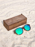 Load image into Gallery viewer, Wenge wooden sunglasses with green polarized lenses and a box on sandy beach.