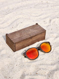 Load image into Gallery viewer, Wenge wooden sunglasses with red polarized lenses and a box on sandy beach.
