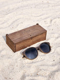 Load image into Gallery viewer, Wenge wooden sunglasses with black polarized lenses and a box on sandy beach.