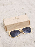 Load image into Gallery viewer, Maple wooden sunglasses with black polarized lenses and a box on sandy beach.