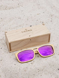 Load image into Gallery viewer, Maple wooden sunglasses with purple polarized lenses and a box on sandy beach.