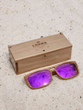 Load image into Gallery viewer, Walnut wooden sunglasses with purple polarized lenses and a box on sandy beach.