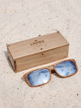 Load image into Gallery viewer, Walnut wooden sunglasses with silver polarized lenses and a box on sandy beach.