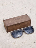Load image into Gallery viewer, Wenge wooden sunglasses with black polarized lenses and a box on sandy beach.