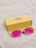 Load image into Gallery viewer, Yellowheart wooden sunglasses with red polarized lenses and a box on sandy beach.