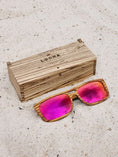 Load image into Gallery viewer, Zebrawood wooden sunglasses with red polarized lenses and a box on sandy beach.