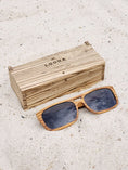 Load image into Gallery viewer, Zebrawood wooden sunglasses with black polarized lenses and a box on sandy beach.