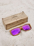 Load image into Gallery viewer, Zebrawood wooden sunglasses with purple polarized lenses and a box on sandy beach.