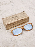 Load image into Gallery viewer, Zebrawood wooden sunglasses with silver polarized lenses and a box on sandy beach.