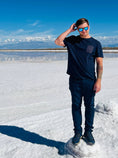 Load image into Gallery viewer, A man standing on a salt flat, wearing purpleheart wood sunglasses with aqua blue polarized lenses.