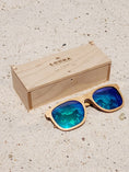Load image into Gallery viewer, Maple wooden sunglasses with green polarized lenses and a box on sandy beach.