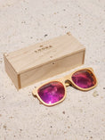 Load image into Gallery viewer, Maple wooden sunglasses with red polarized lenses and a box on sandy beach.