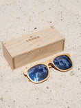 Load image into Gallery viewer, Maple wooden sunglasses with silver polarized lenses and a box on sandy beach.