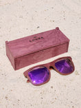 Load image into Gallery viewer, Purpleheart wooden sunglasses with purple polarized lenses and a box on sandy beach.