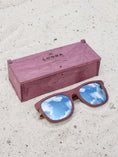 Load image into Gallery viewer, Purpleheart wooden sunglasses with silver polarized lenses and a box on sandy beach.