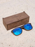 Load image into Gallery viewer, Wenge wooden sunglasses with bluek polarized lenses and a box on sandy beach.