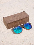 Load image into Gallery viewer, Wenge wooden sunglasses with green polarized lenses and a box on sandy beach.