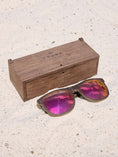 Load image into Gallery viewer, Wenge wooden sunglasses with red polarized lenses and a box on sandy beach.