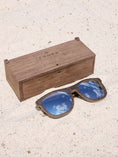 Load image into Gallery viewer, Wenge wooden sunglasses with silver polarized lenses and a box on sandy beach.