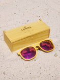 Load image into Gallery viewer, Yellowheart wooden sunglasses with red polarized lenses and a box on sandy beach.