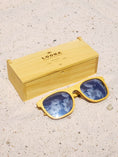 Load image into Gallery viewer, Yellowheart wooden sunglasses with silver polarized lenses and a box on sandy beach.