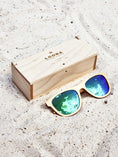 Load image into Gallery viewer, Maple wooden sunglasses with green polarized lenses and a box on sandy beach.