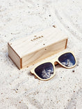 Load image into Gallery viewer, Maple wooden sunglasses with black polarized lenses and a box on sandy beach.