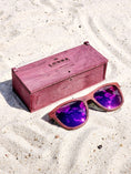 Load image into Gallery viewer, Purpleheart wooden sunglasses with purple polarized lenses and a box on sandy beach.