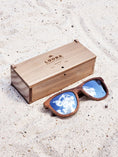 Load image into Gallery viewer, Walnut wooden sunglasses with silver polarized lenses and a box on sandy beach.