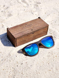 Load image into Gallery viewer, Wenge wooden sunglasses with blue polarized lenses and a box on sandy beach.