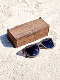 Load image into Gallery viewer, Wenge wooden sunglasses with black polarized lenses and a box on sandy beach.
