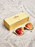 Load image into Gallery viewer, Yellowheart wooden sunglasses with red polarized lenses and a box on sandy beach.