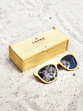 Load image into Gallery viewer, Yellowheart wooden sunglasses with black polarized lenses and a box on sandy beach.