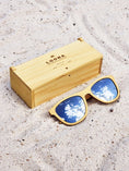 Load image into Gallery viewer, Yellowheart wooden sunglasses with silver polarized lenses and a box on sandy beach.