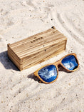 Load image into Gallery viewer, Zebrawood wooden sunglasses with silver polarized lenses and a box on sandy beach.