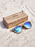 Load image into Gallery viewer, Zebrawood wooden sunglasses with blue polarized lenses and a box on sandy beach.
