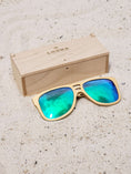 Load image into Gallery viewer, Maple wooden sunglasses with green polarized lenses and a box on sandy beach.