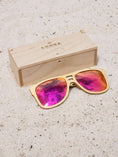 Load image into Gallery viewer, Maple wooden sunglasses with red polarized lenses and a box on sandy beach.