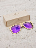 Load image into Gallery viewer, Maple wooden sunglasses with purple polarized lenses and a box on sandy beach.