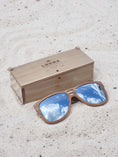 Load image into Gallery viewer, Walnut wooden sunglasses with silver polarized lenses and a box on sandy beach.
