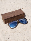 Load image into Gallery viewer, Wenge wooden sunglasses with silver polarized lenses and a box on sandy beach.