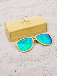 Load image into Gallery viewer, Yellowheart wooden sunglasses with green polarized lenses and a box on sandy beach.