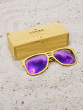 Load image into Gallery viewer, Yellowheart wooden sunglasses with purple polarized lenses and a box on sandy beach.