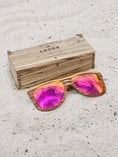 Load image into Gallery viewer, Zebrawood wooden sunglasses with red polarized lenses and a box on sandy beach.