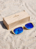 Load image into Gallery viewer, Maple wooden sunglasses with blue polarized lenses and a box on sandy beach.