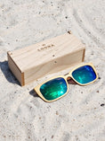 Load image into Gallery viewer, Maple wooden sunglasses with green polarized lenses and a box on sandy beach.