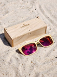 Load image into Gallery viewer, Maple wooden sunglasses with red polarized lenses and a box on sandy beach.